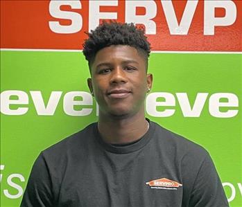 Male employee Malike Cooper standing in front of a green wall with SERVPRO logo.