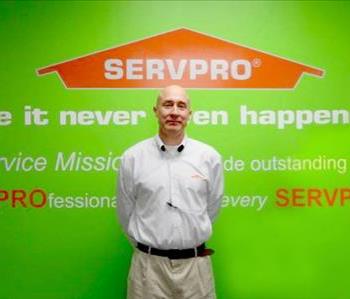 Mark Mitchell standing in front of a green wall with the SERVPRO logo and mission statement below it.