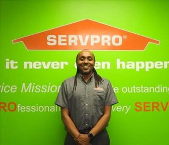 Eric Mwangi standing in front of a green wall with the SERVPRO logo and mission statement below it.