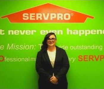 Sarah Raymond standing in front of a green wall with the SERVPRO logo and mission statement below it.